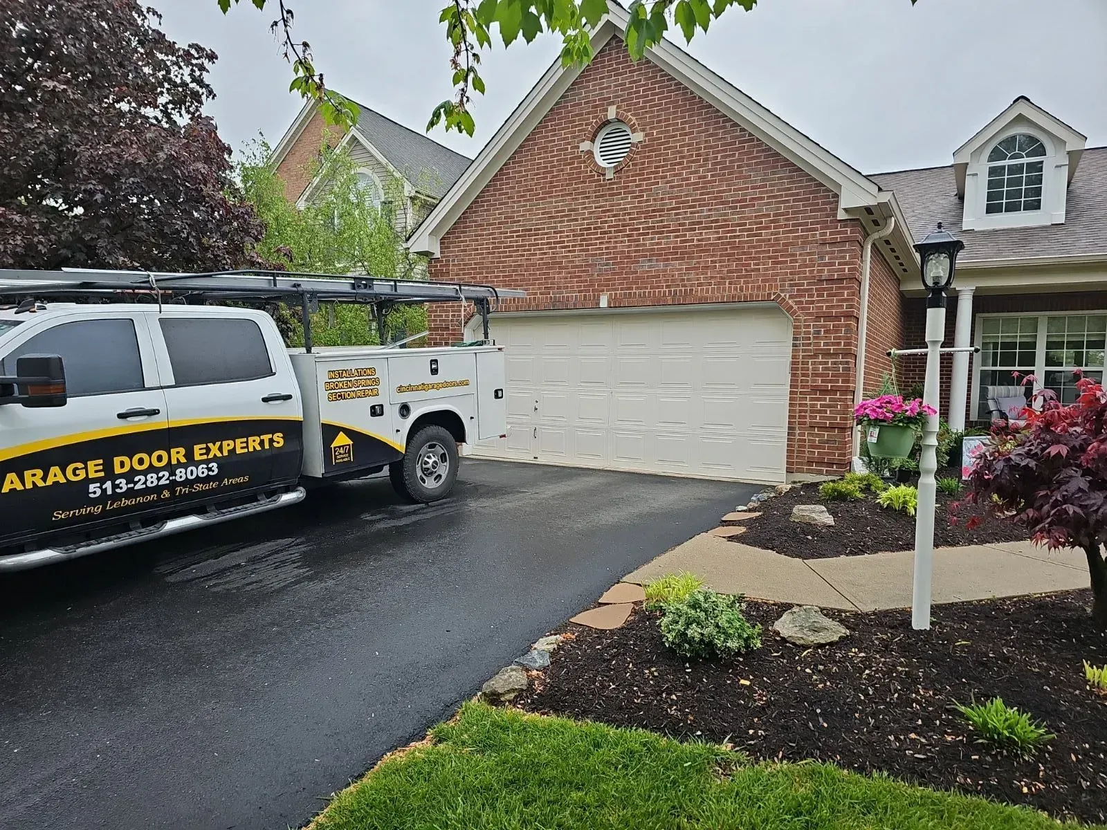 Garage door repair truck parked by a brick house with a closed white garage door