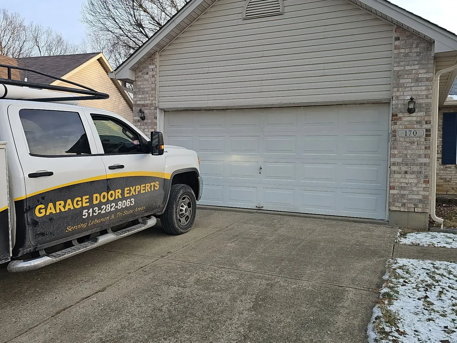 Garage door repair truck parked in front of a suburban house with a white garage door.