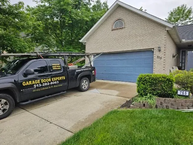 Garage Door Experts truck parked in a driveway beside a house with a blue garage door.