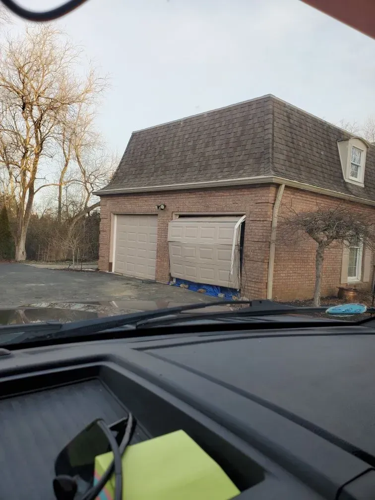 Car parked facing a brick garage with closed doors on a driveway, viewed from inside another car