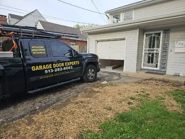 Garage Door Experts van parked beside a house’s open garage, with a driveway and lawn in front.