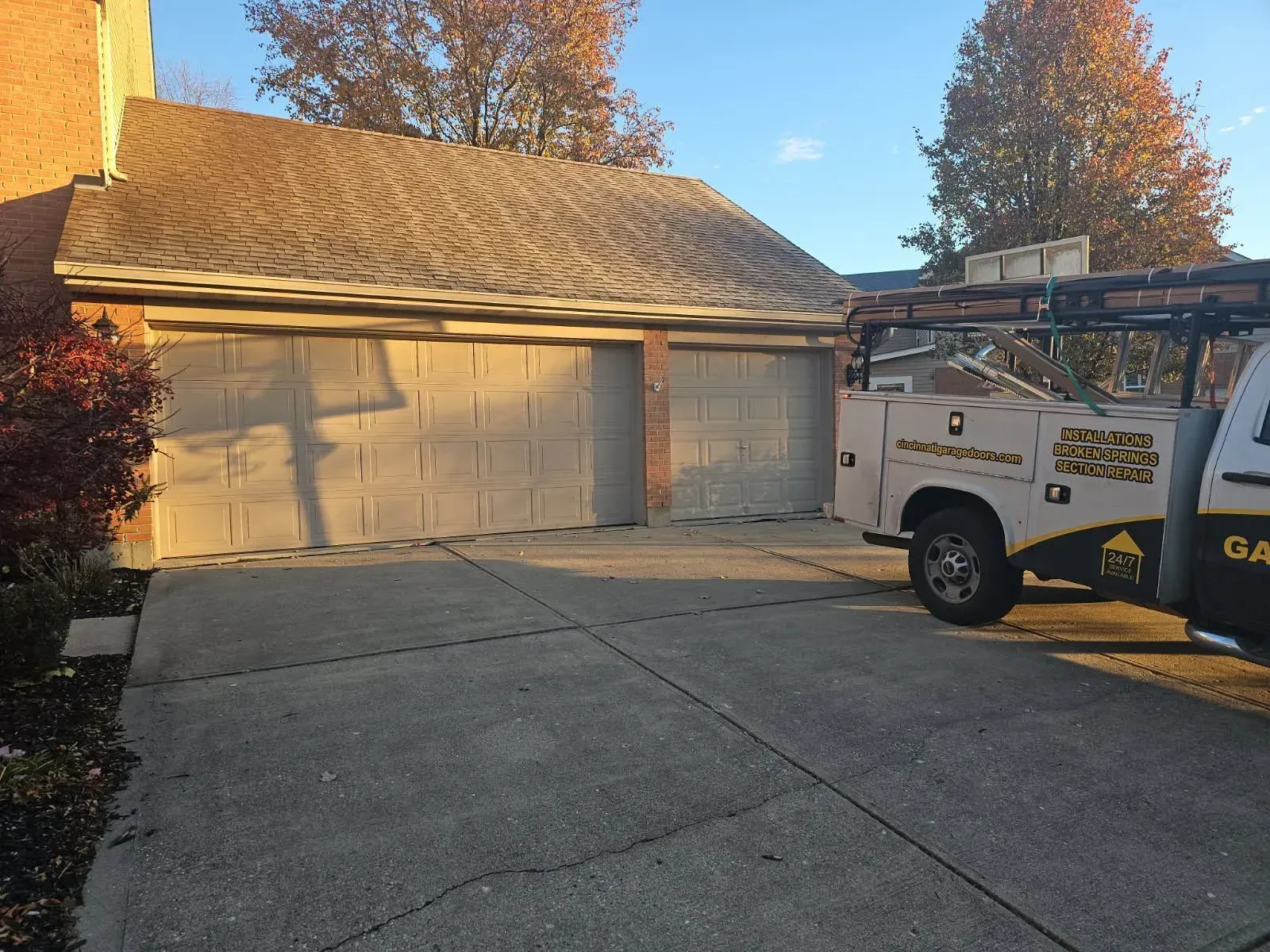 White garage with closed doors and a utility truck parked in a driveway at sunset.
