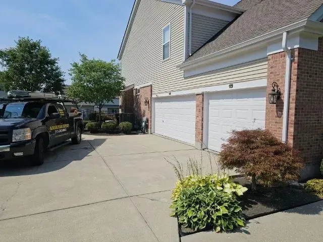 Suburban house driveway with white garage doors, a parked SUV, and landscaped shrubs