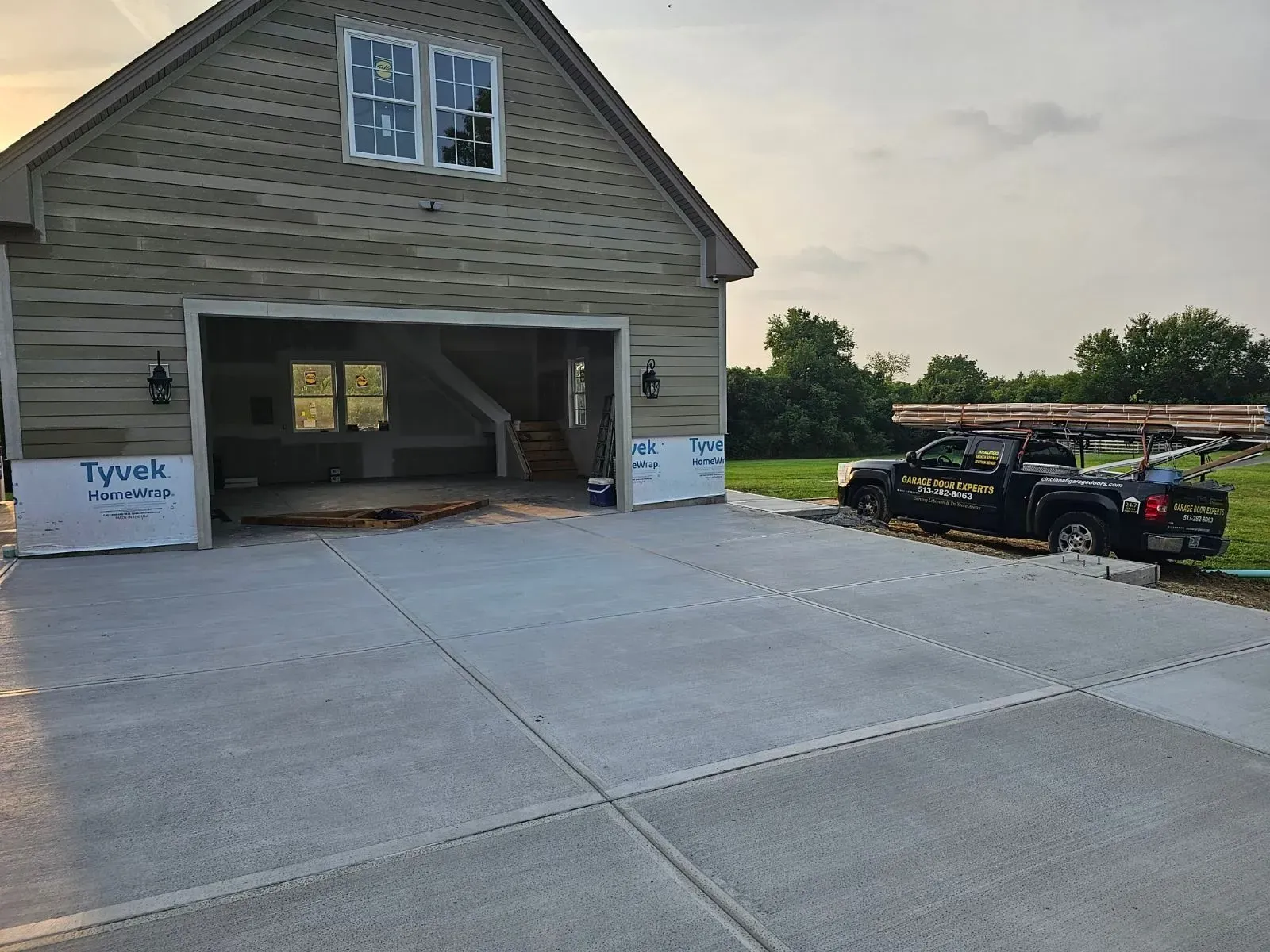 New house with open garage, concrete driveway, and black pickup truck parked beside it
