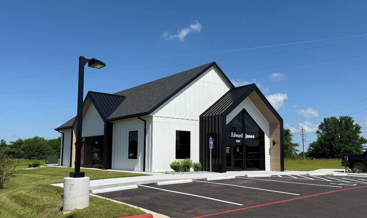 White and black modern building with a dark roof, next to a paved parking lot and blue sky.