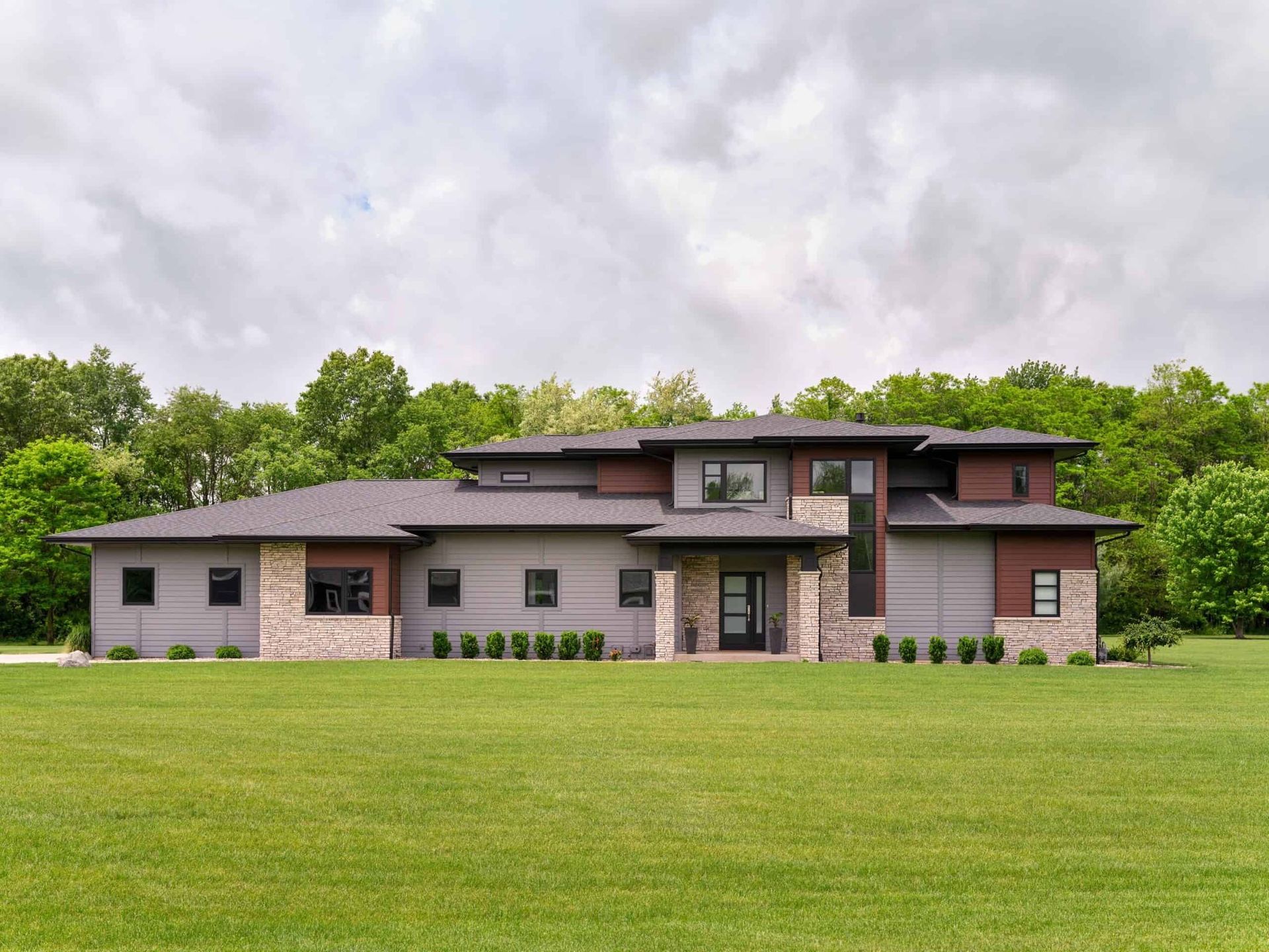 Modern home with gray and brown exterior, surrounded by green lawn and trees.
