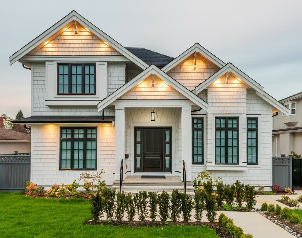 White two-story house with black-trimmed windows, a dark front door, and manicured lawn; evening view.