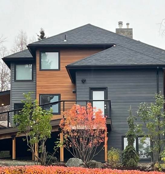Two-story house with gray and wood siding, black-framed windows, and a deck surrounded by autumn foliage.