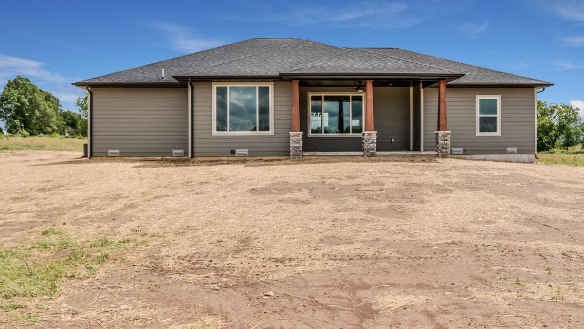 Back of a gray house with covered patio, set on a gravel yard under a blue sky.