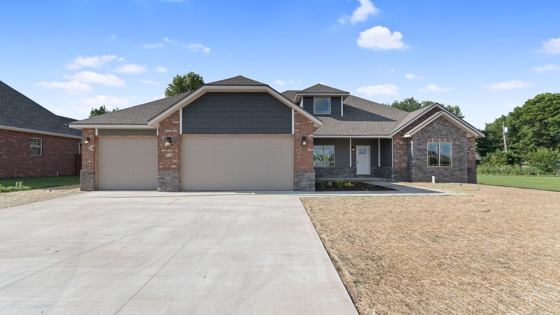 Tan brick and stone house with a two-car garage on a concrete driveway. Blue sky with scattered clouds.