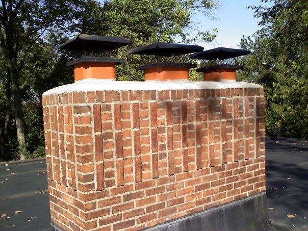 A brick chimney on top of a roof with trees in the background