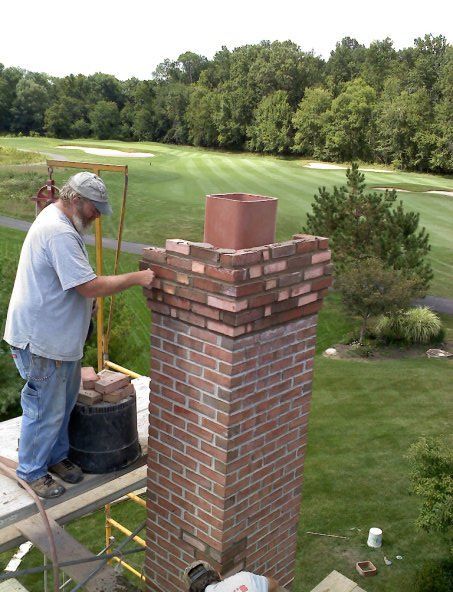 A man is working on a brick chimney with a golf course in the background