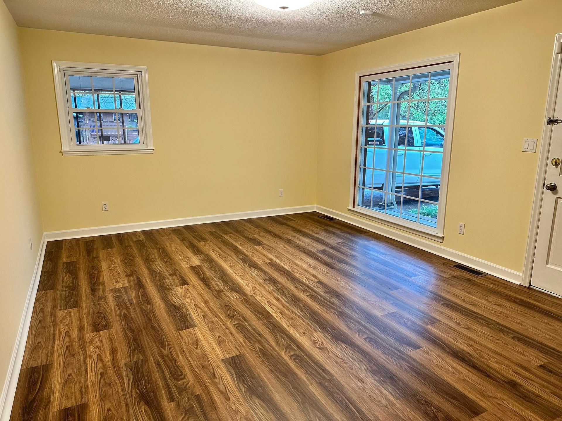 Empty room with hardwood floors, a small window, and a sliding glass door. Yellow walls.