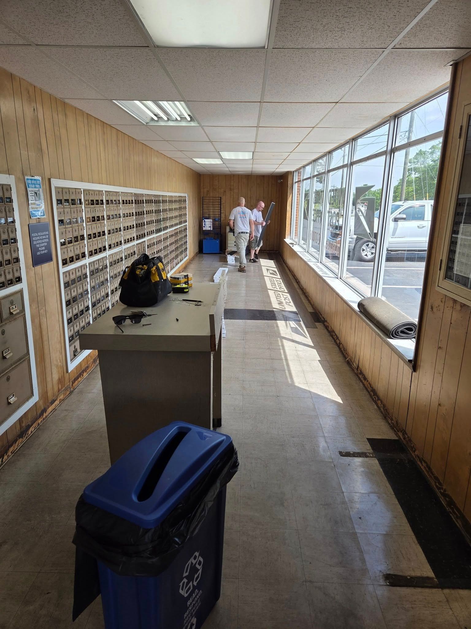 Interior of a post office with mailboxes, counter, and two people walking towards the end of the hall.