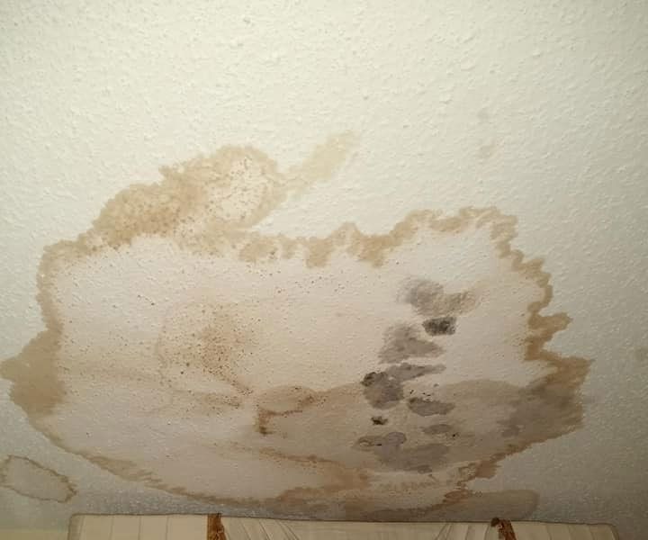 Water stain on a white ceiling, brown and discolored, with a defined circular shape, indicating a leak.