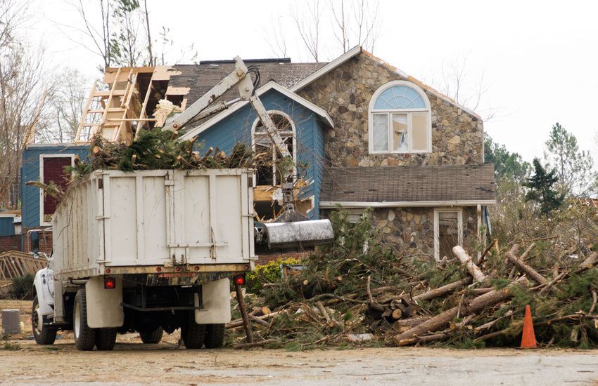 Truck loading tree debris from house with roof damage.