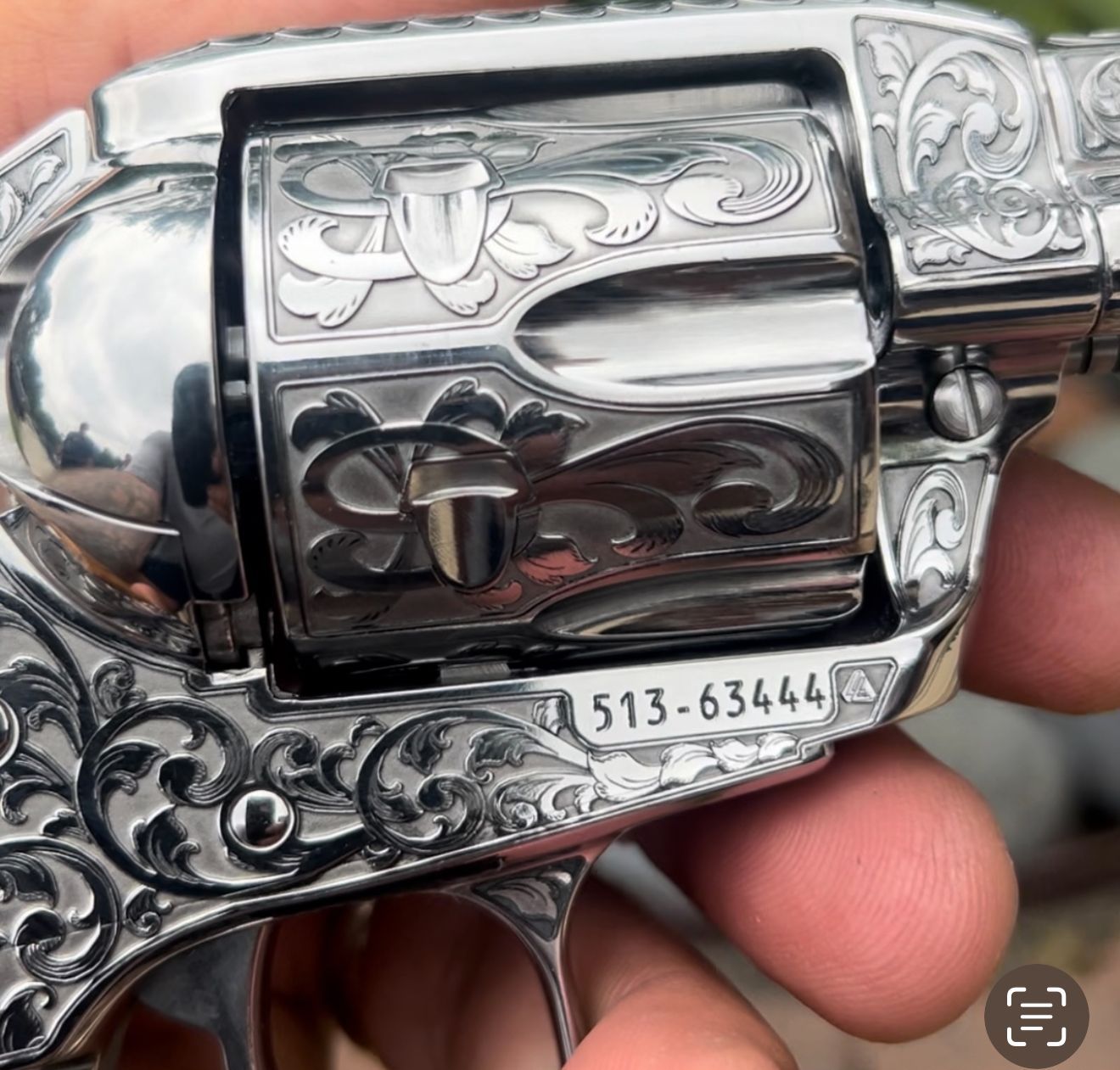 A person is holding a silver revolver with the number 513-63444 on it
