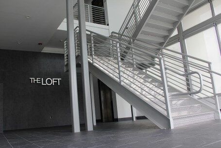 A staircase in a building with a railing and a sign that says The Loft