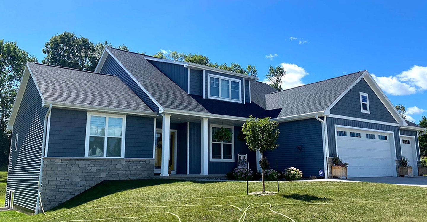 A black house with a gray roof and white trim is surrounded by trees