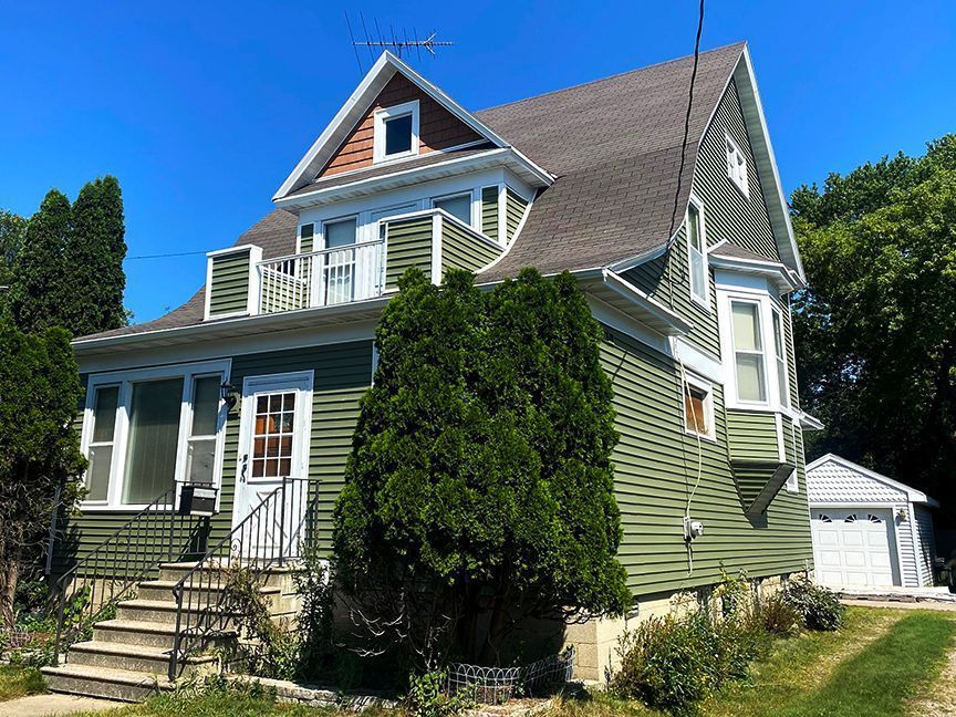 A large house with a green siding and a brown roof