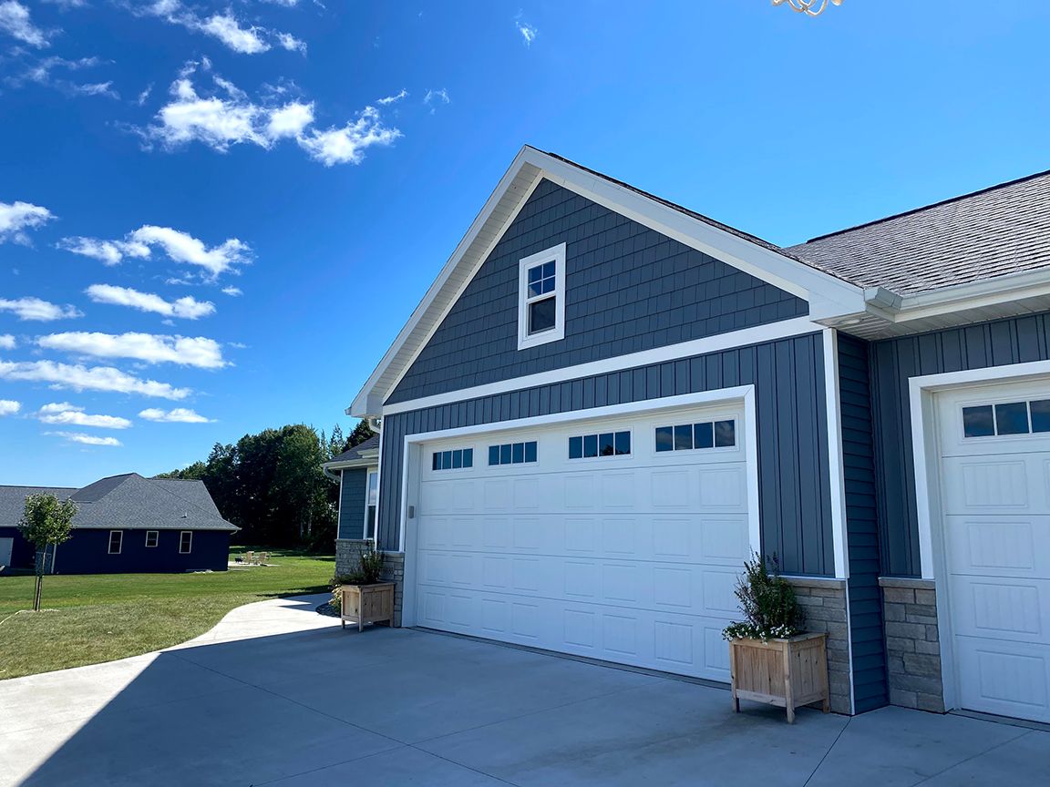 A house with two garage doors and a blue siding on a sunny day.