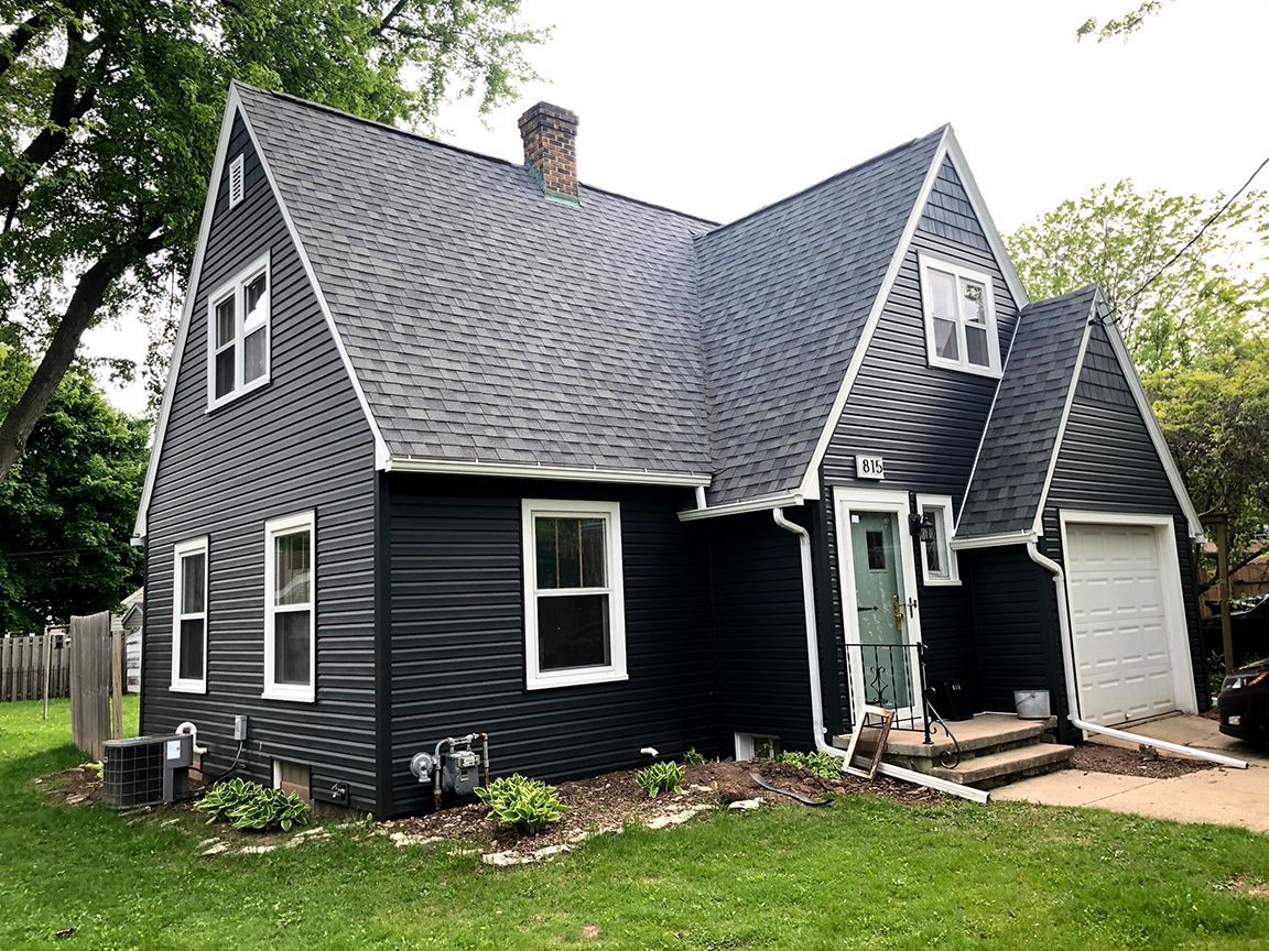 A black house with white trim and a garage is sitting on top of a lush green lawn.