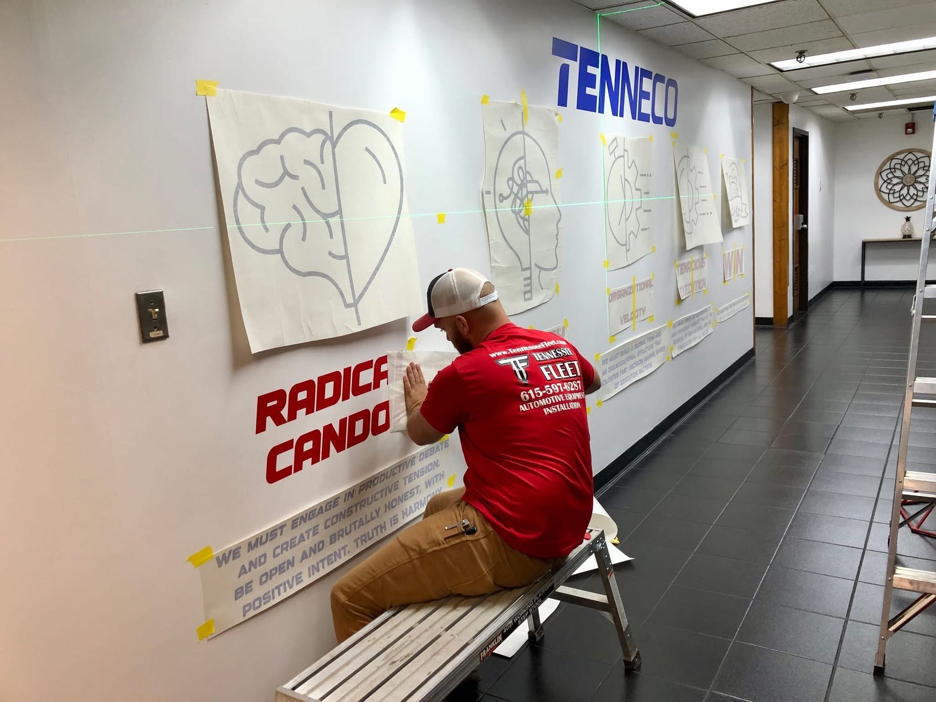 A man is sitting on a bench in a hallway painting a wall mural.