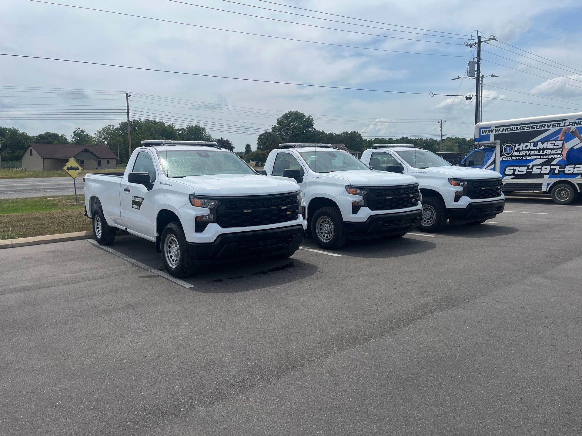 Three white pickup trucks are parked in a parking lot.