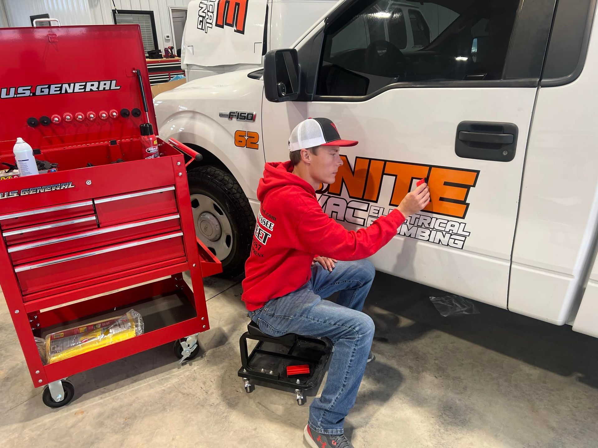A man in a red hoodie is kneeling down next to a white truck.