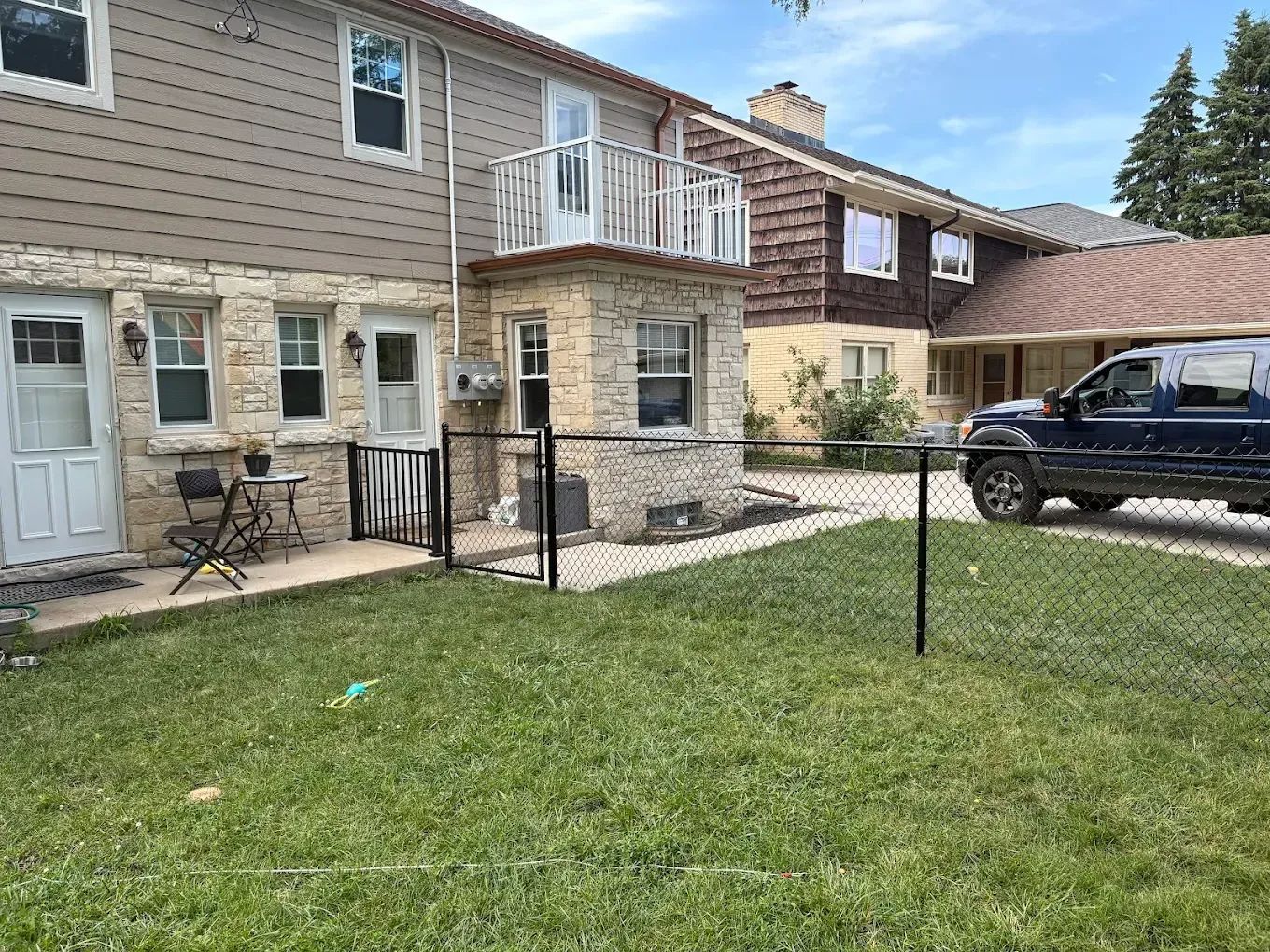 Row of connected houses with a fenced yard and a parked blue SUV. Green grass and overcast sky.