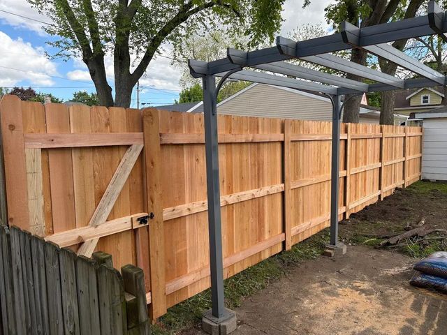 Wooden fence with a gate, metal pergola, and a patch of yard.
