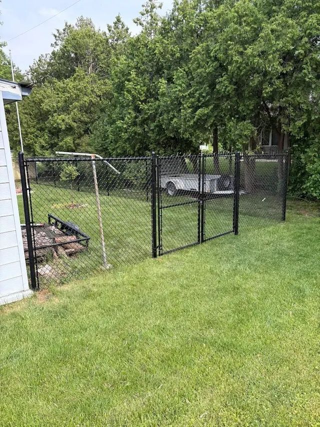 Black chain-link fence with gates encloses a grassy backyard area; trees in the background.
