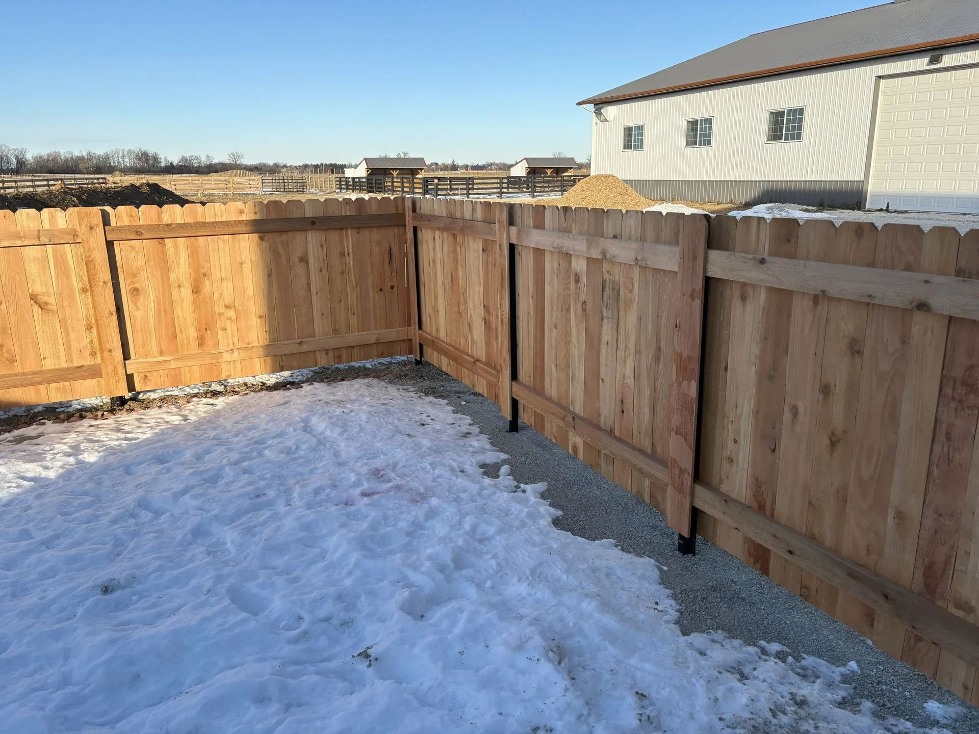 Wooden fence surrounding a snow-covered area, with a building in the background.