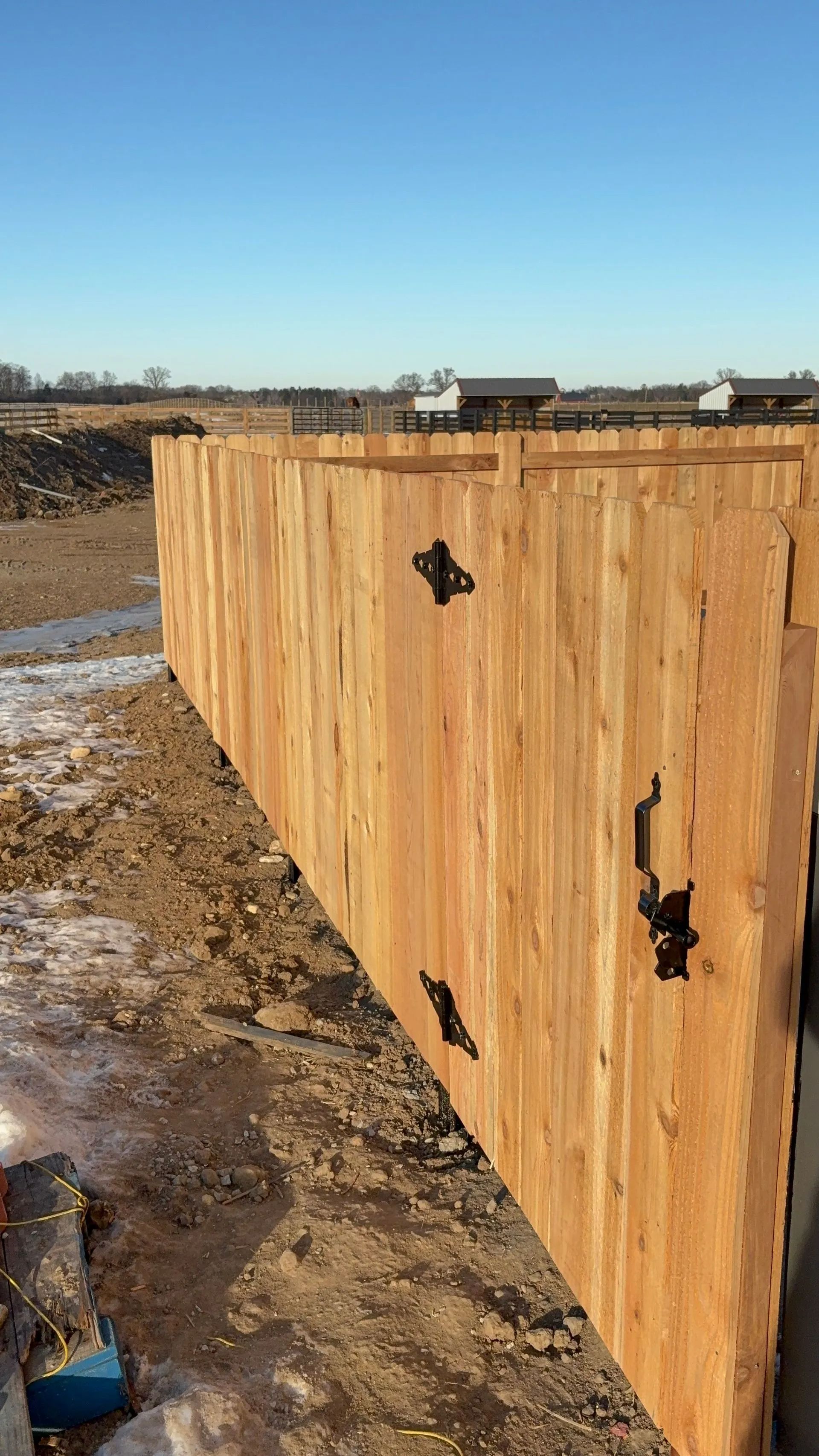 Wooden fence panels in a dirt lot, black hardware visible, under a clear blue sky.