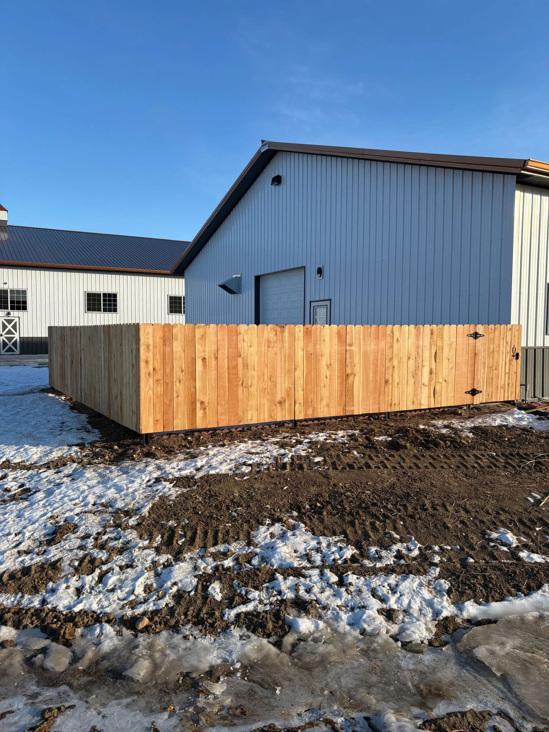 Wooden fence in front of a white building with a black roof, in a snowy outdoor setting.