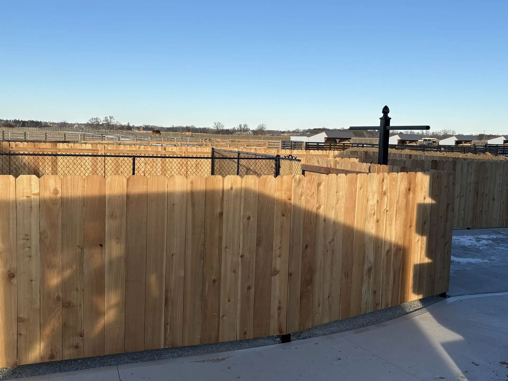 Wooden fence surrounding an area, with chain-link fence visible in the distance under a blue sky.