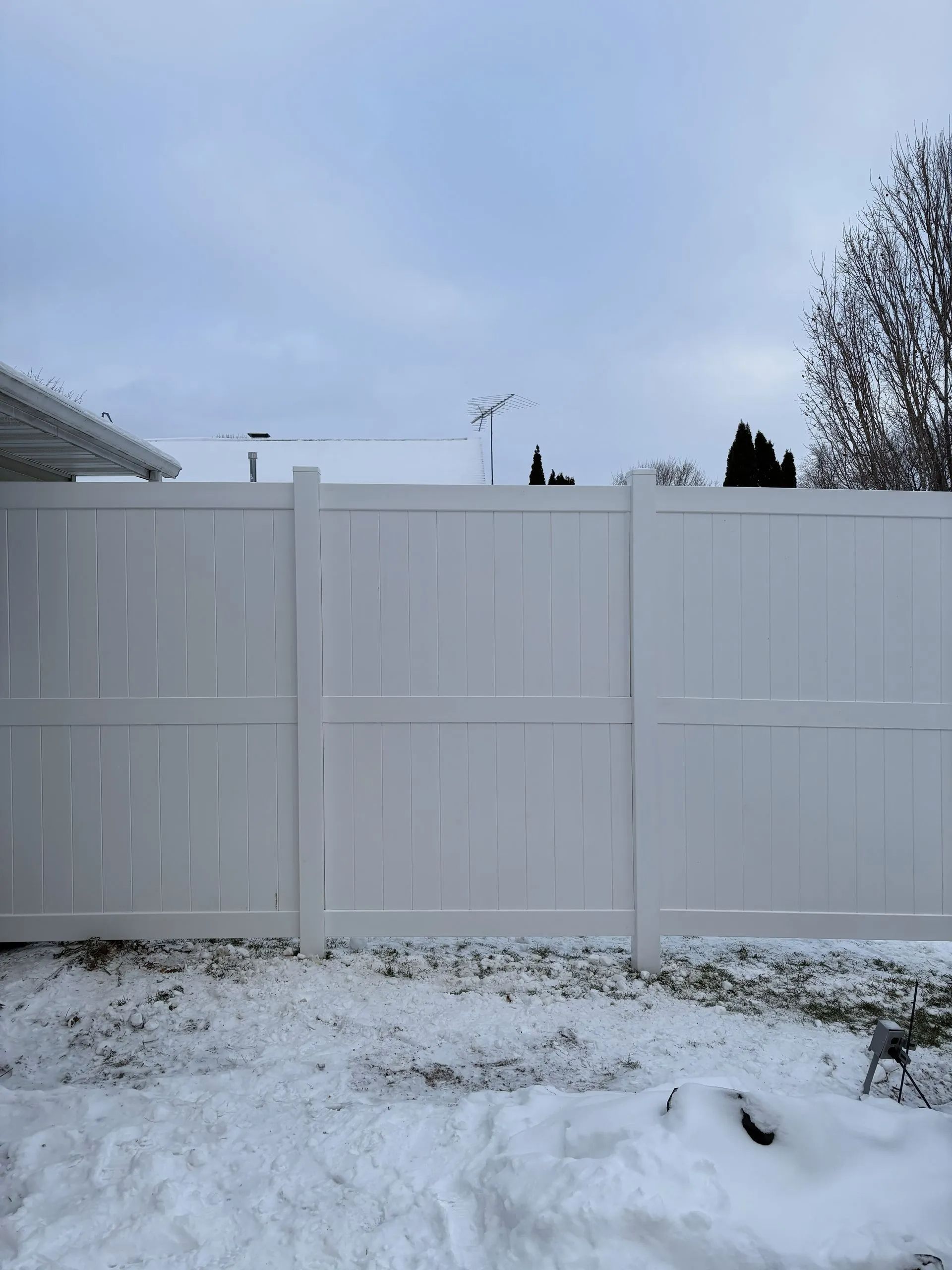 White vinyl fence in a snow-covered yard on a cloudy day.