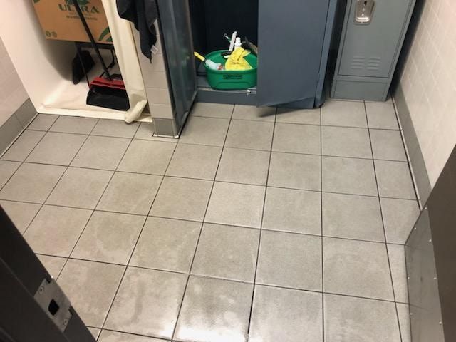 Gray tiled floor in front of a partially open gray cabinet with cleaning supplies inside.