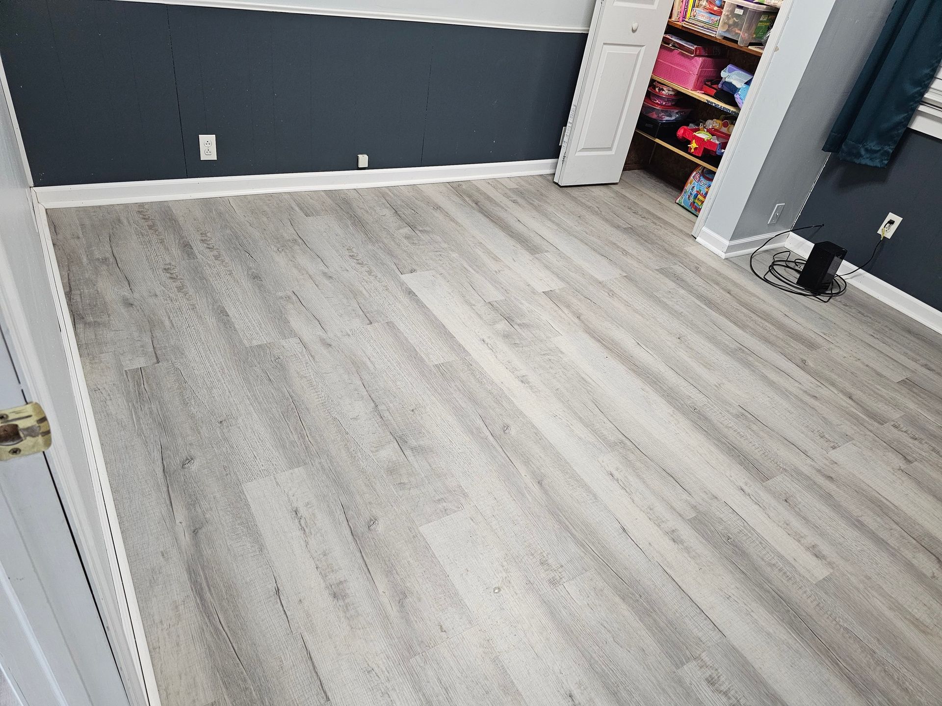 Gray wood-look flooring in a room with blue walls, a white door, and a partially visible closet.