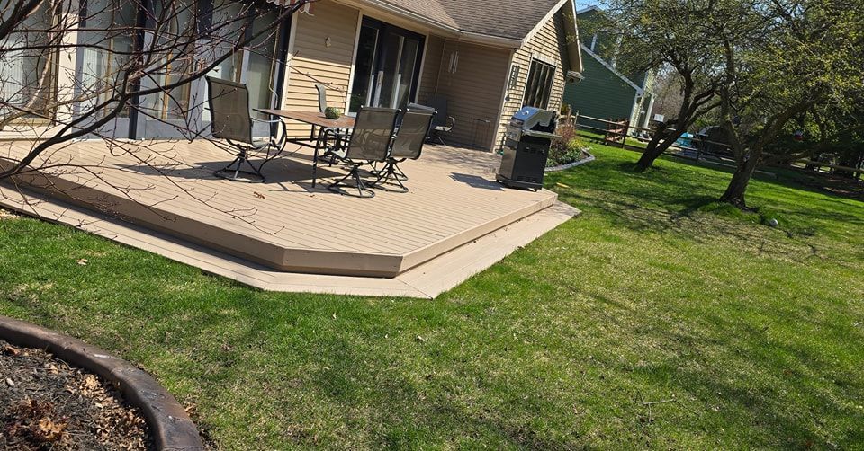 A backyard patio with outdoor furniture, a grill, and a grassy lawn.