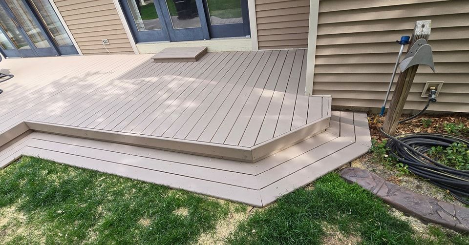 Composite deck with steps, tan color, next to a beige siding house and green grass.