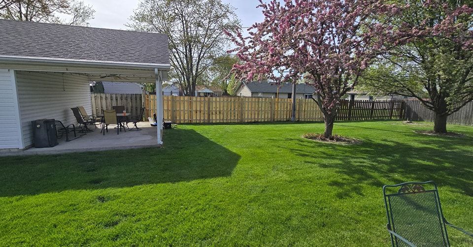Backyard with green grass, patio, wooden fence, and flowering tree.