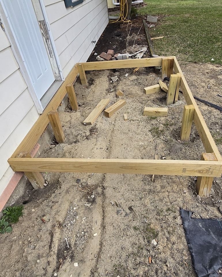 Wooden deck frame under construction next to a beige house and dirt.