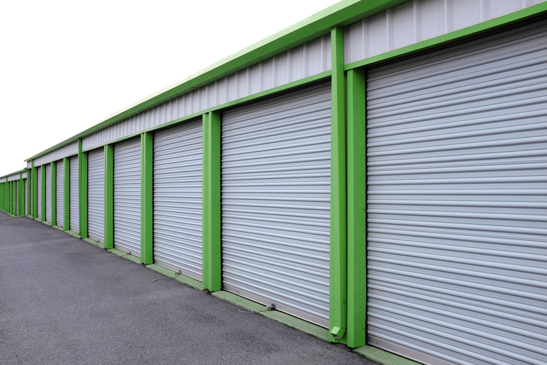 Row of green-trimmed metal storage unit doors along a paved alley