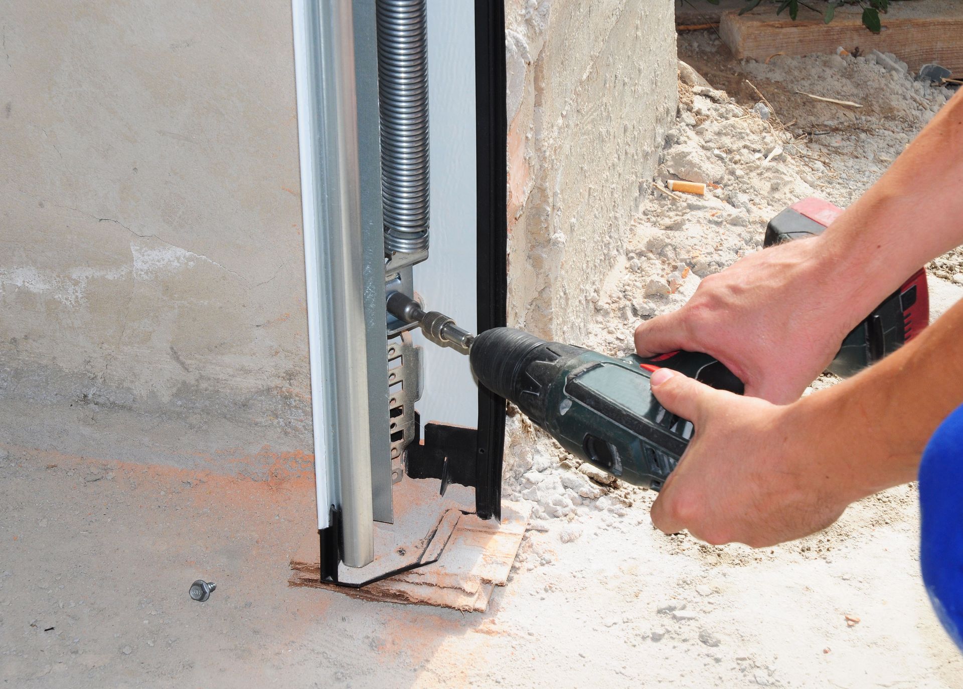 Hands using a power drill to fasten a metal frame to a concrete wall outdoors