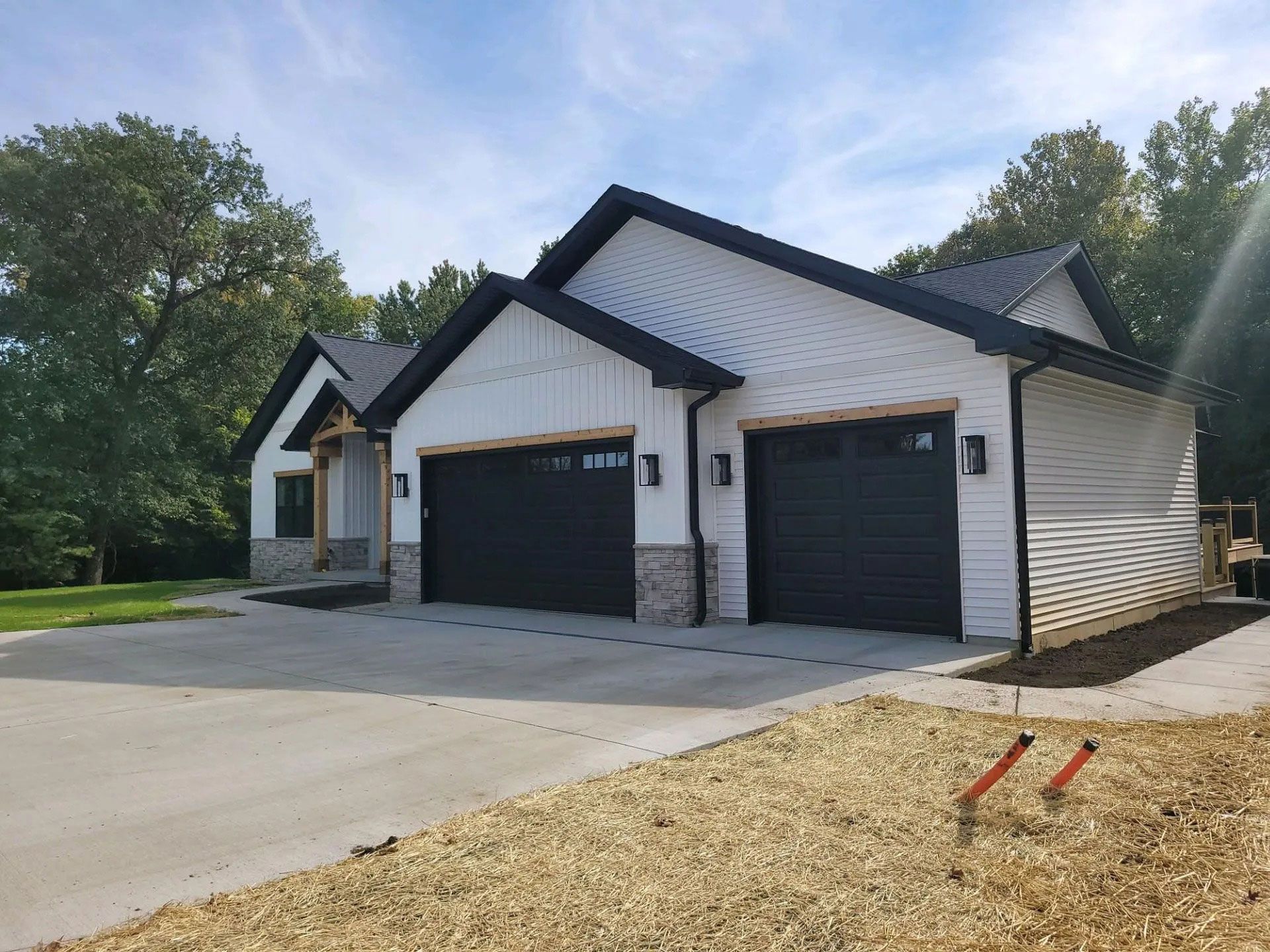 White house with two black garage doors and a concrete driveway beside a grassy yard and trees