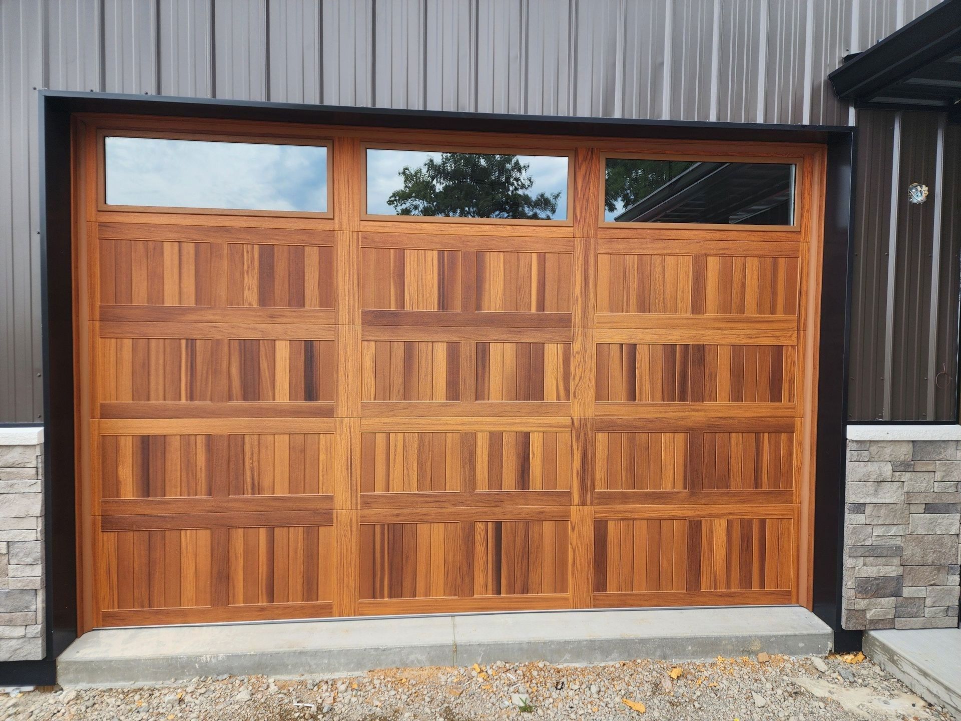 Wooden garage door with small windows, set in a stone and metal exterior wall.