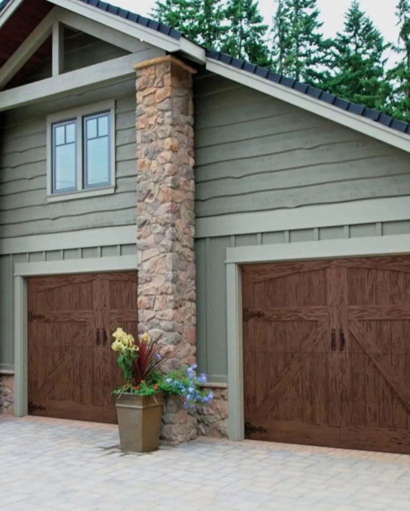 Stone-front house with two wooden garage doors and a flower pot by the driveway