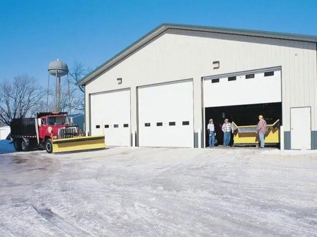 Fire truck and people outside a white garage with open bay doors on a snowy day