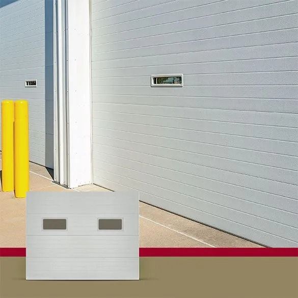 Gray industrial garage door with a small window beside yellow bollards and a curb.